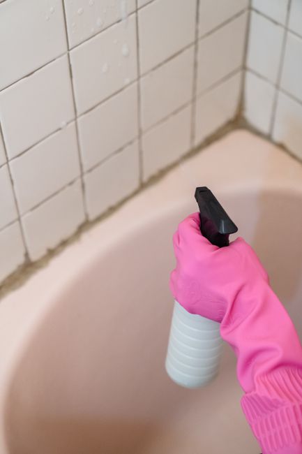 A close-up of a person's hand holding a yellow cleaning cloth with a black border, pressed against a yellow surface, likely a countertop or tabletop, demonstrating surface cleaning. The background is